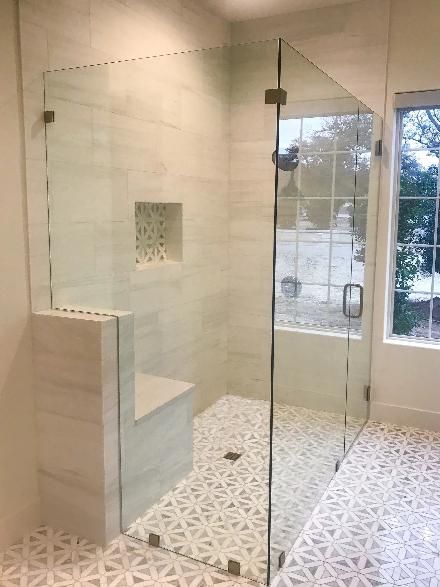 A frameless corner glass shower with a built-in marble bench, a recessed niche and a patterned marble mosaic floor.