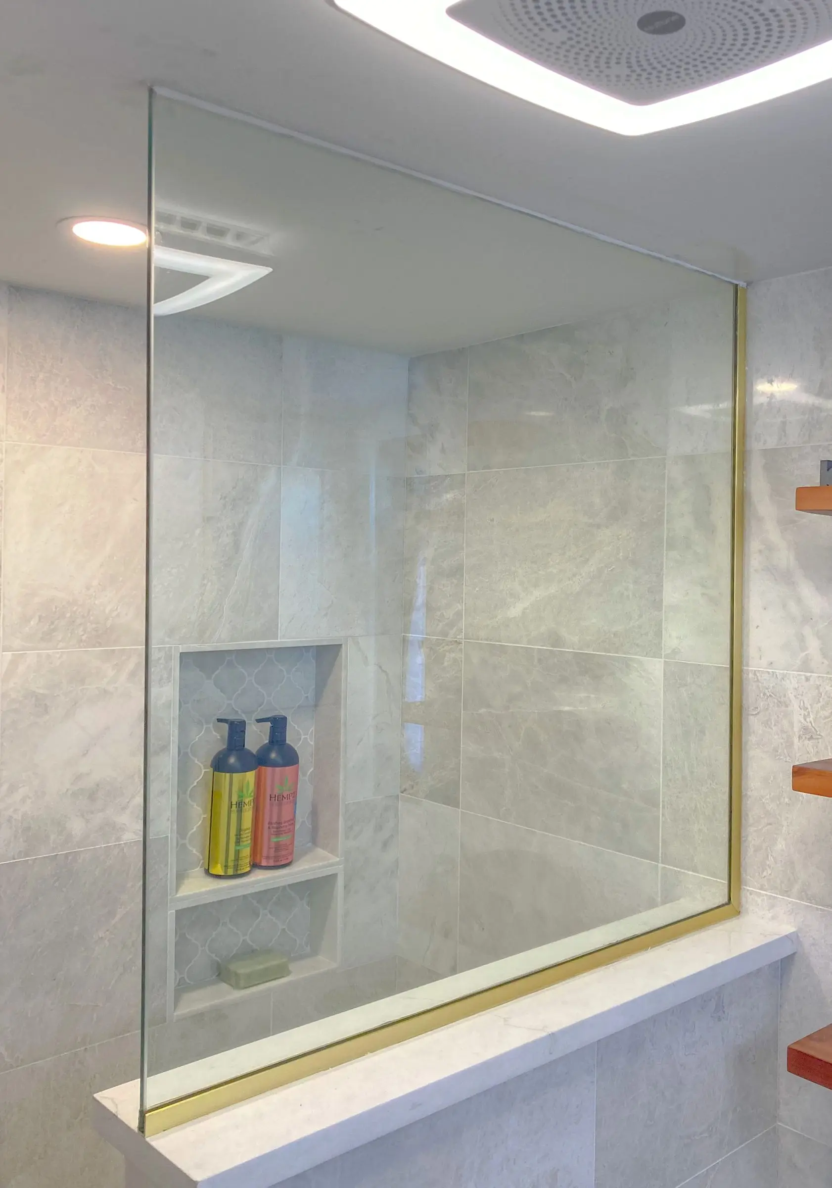 A frameless glass shower enclosure in a marble bathroom with gold-trimmed hardware.