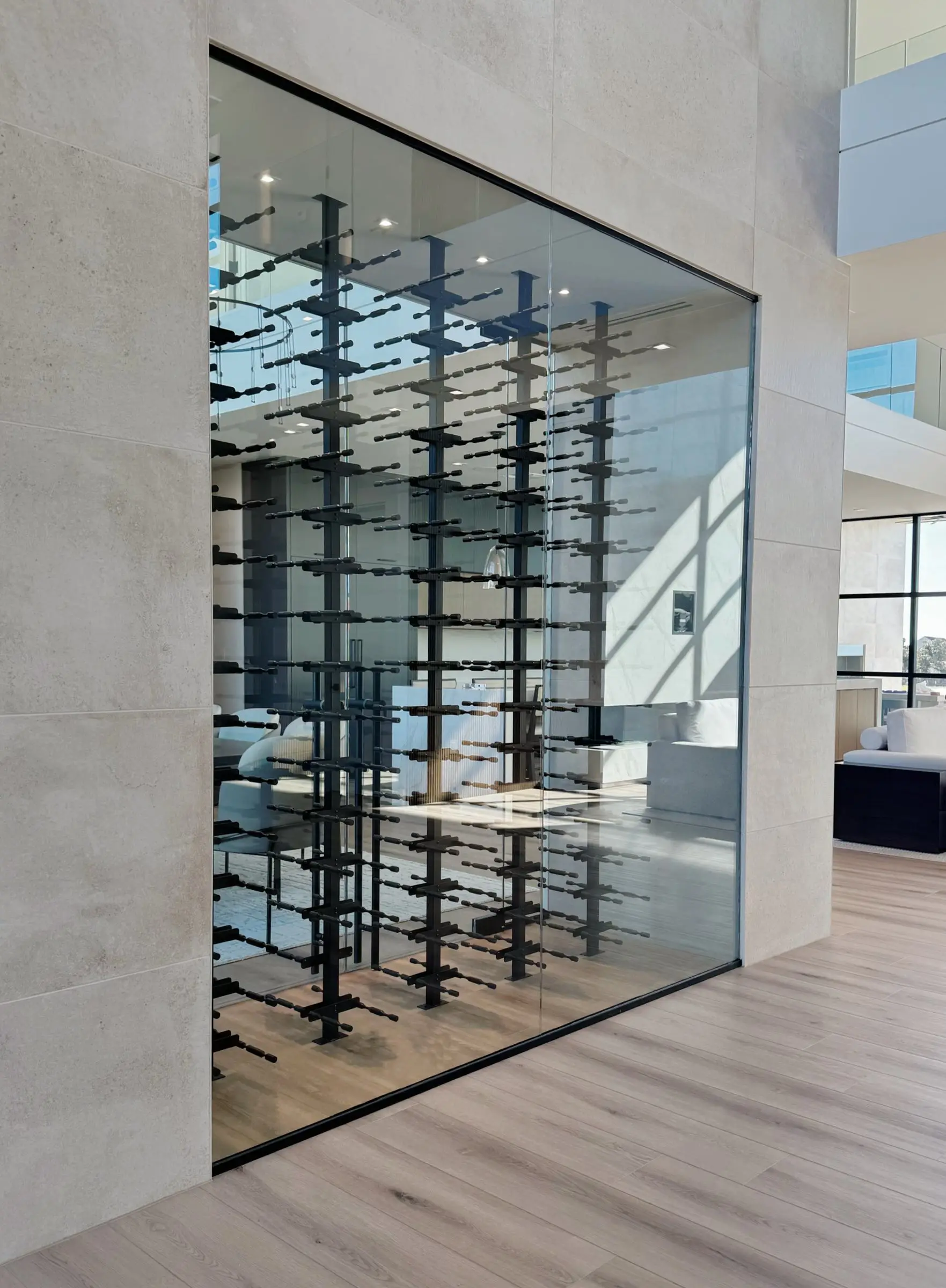 A full-height frameless glass wine room set into a limestone wall, with black metal racks holding bottles on view.