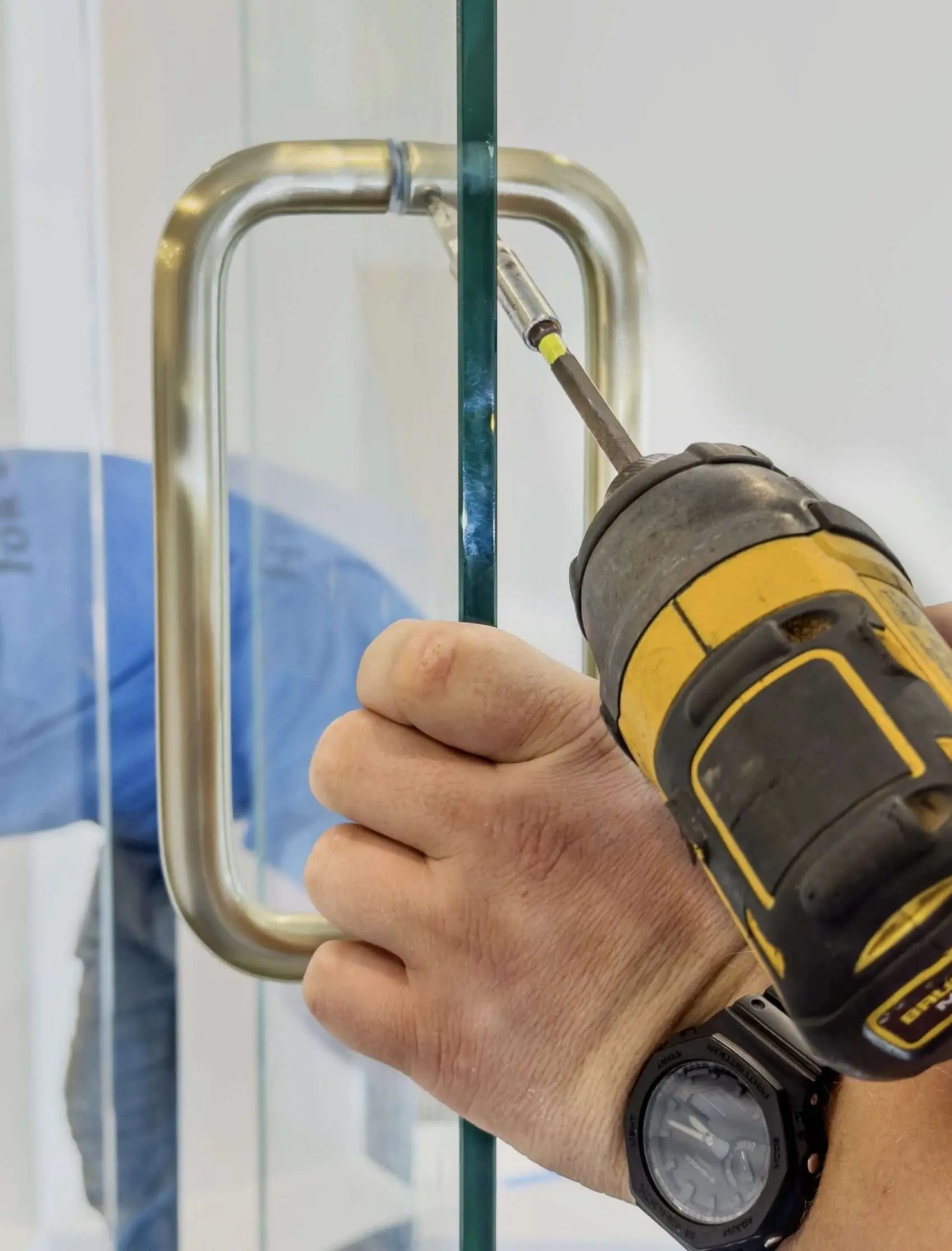 Installer drilling a handle onto a glass shower door.