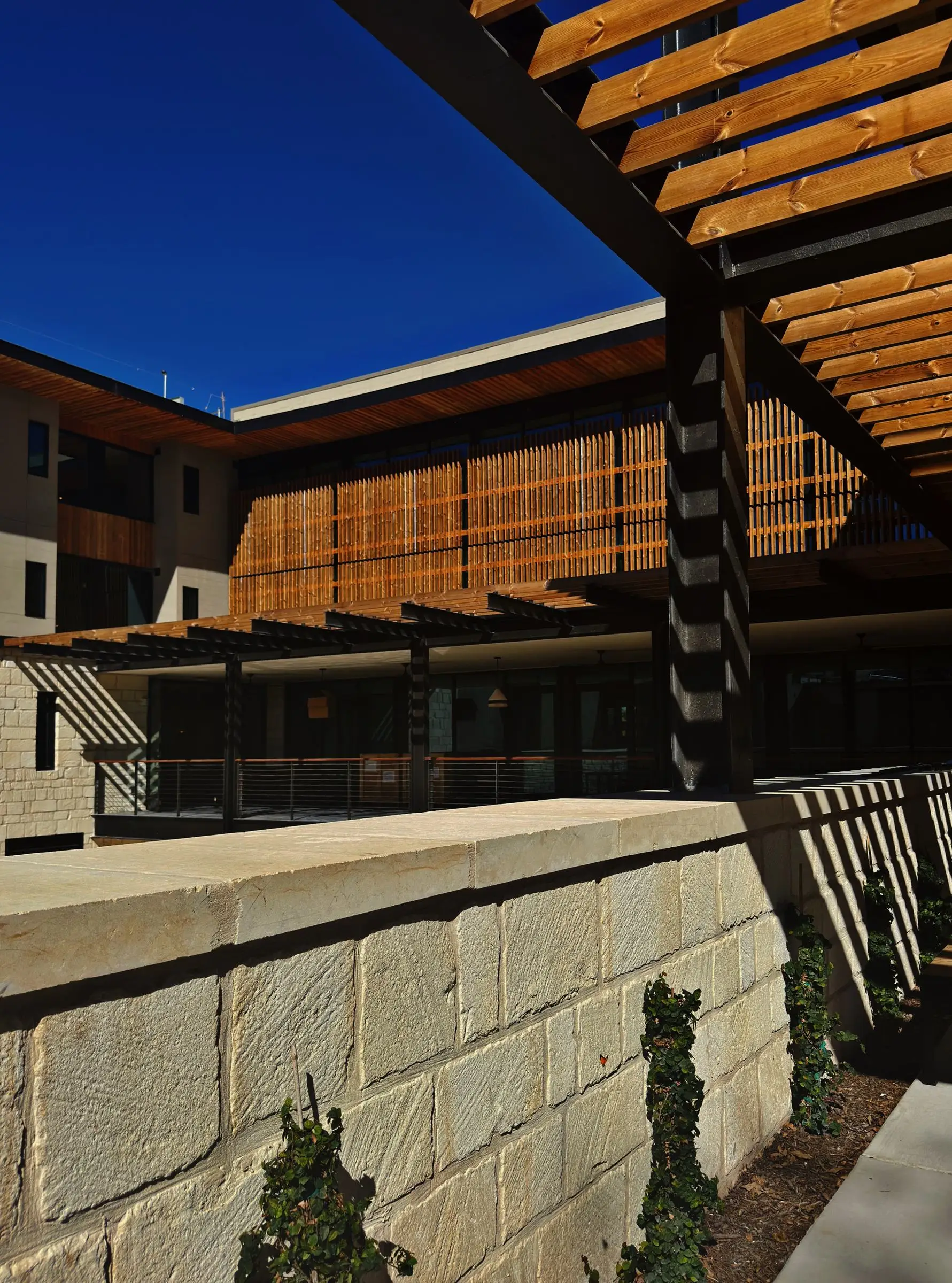 A limestone commercial courtyard with a steel and wood pergola over a covered walkway, and glazed storefront along one side.